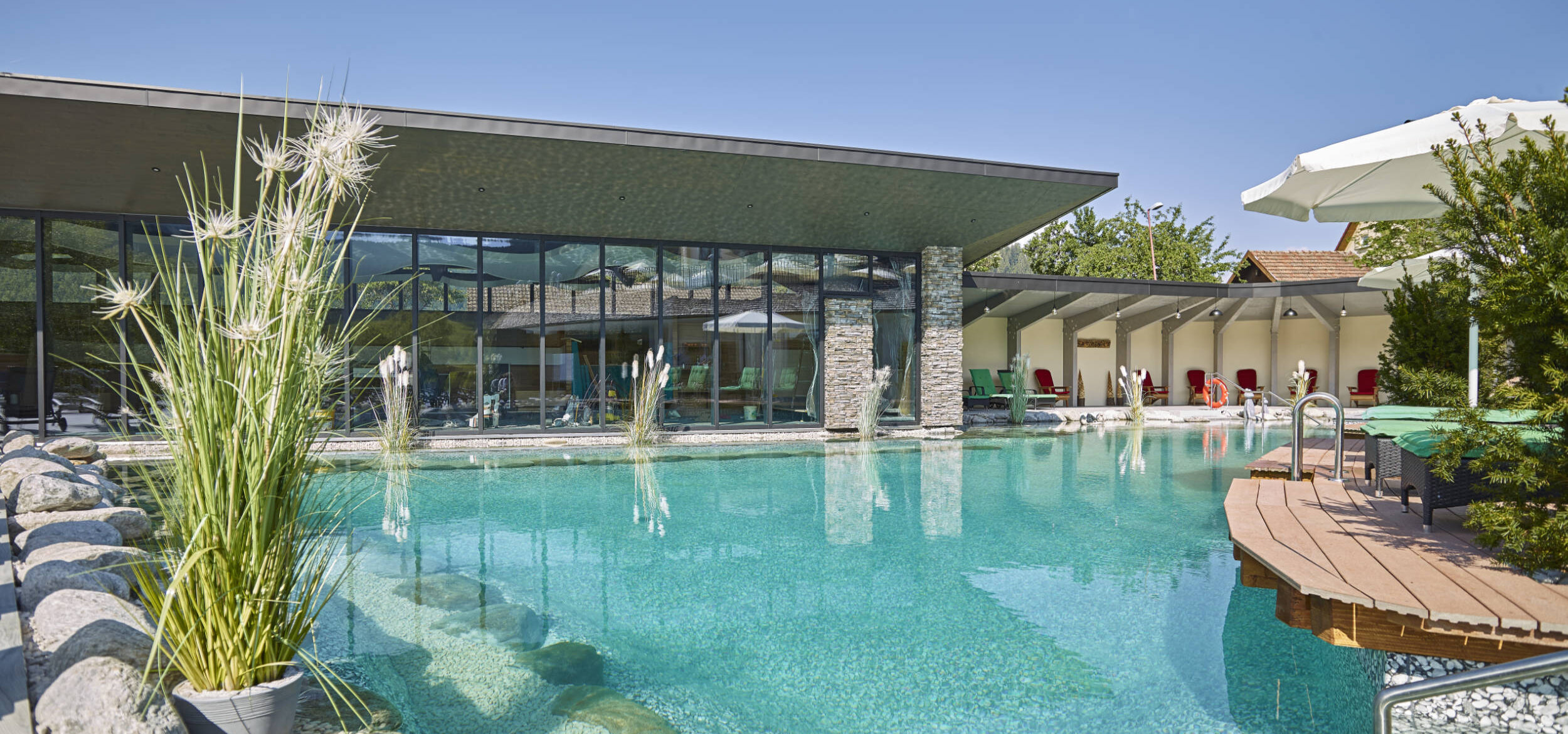 Large swimming pond with Balena system and plants at the “Heselbacher Hof” wellness hotel in Baiersbronn, with the hotel in the background
