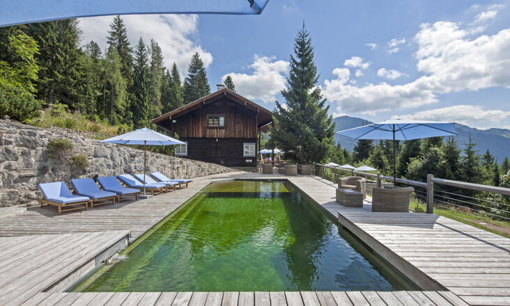 Natural pool with Balena system with loungers at the “Silberghaus” hotel spa in Bayrischzell, with the Alps in the background