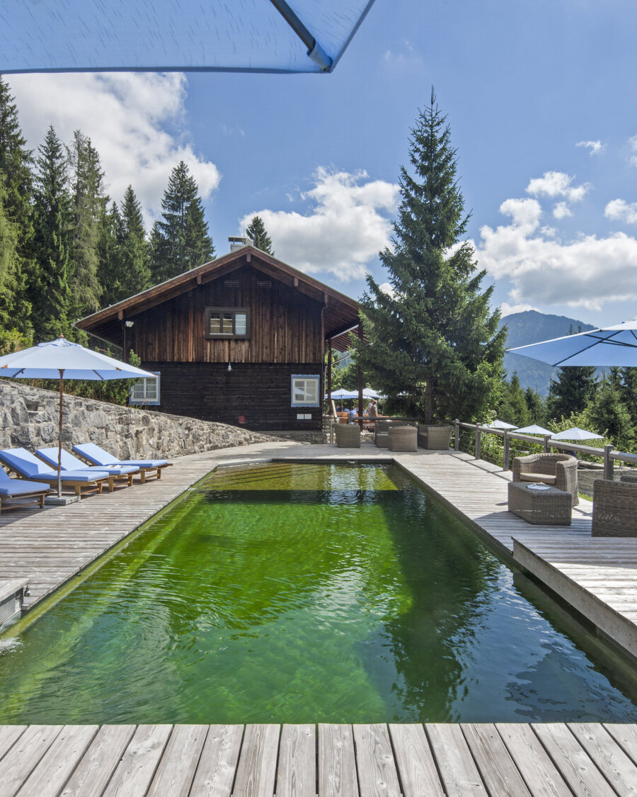 Natural pool with Balena system with loungers at the “Silberghaus” hotel spa in Bayrischzell, with the Alps in the background