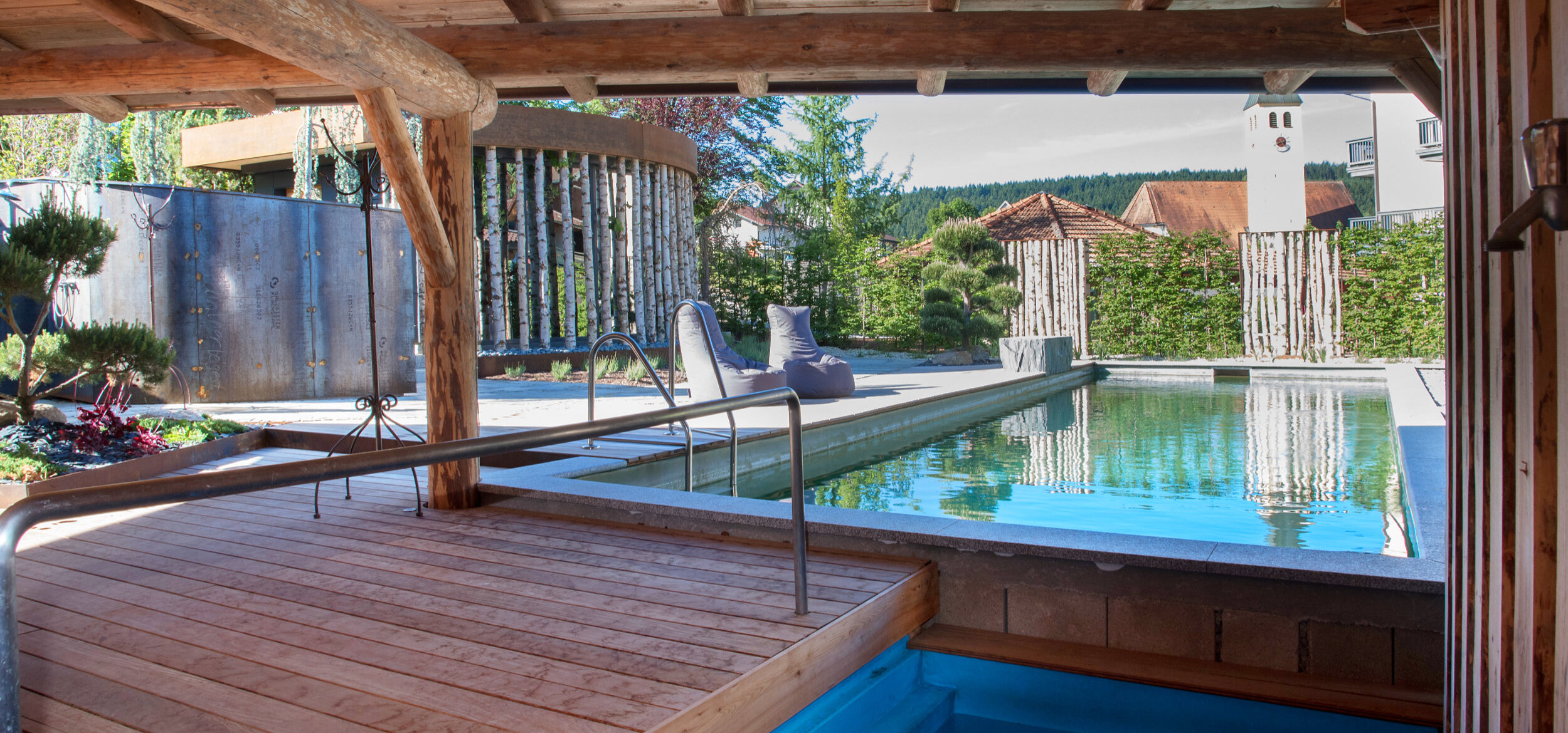 The outdoor area of the wellness & family hotel “Zum Kramerwirt” with whirlpool and canopy, with the Balena natural pool with seating in the background