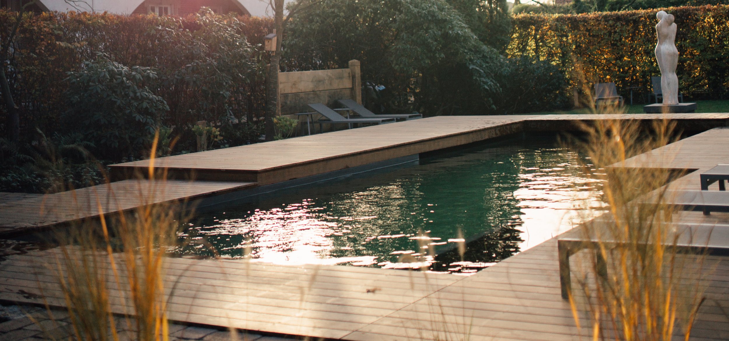 The natural pool with Balena system at the Hotel-Residence “Klosterpforte” in Marienfeld with loungers, plants in the foreground